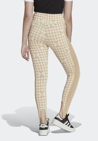 Legíny v béžovém kostkovaném vzoru se vzory hvězd, s vysokým pasem a bočními výřezy, doplněné černými teniskami.