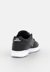Black New Balance sneaker with white sole, "new balance" text on heel, visible "N" logo on side, shown from rear angle.
