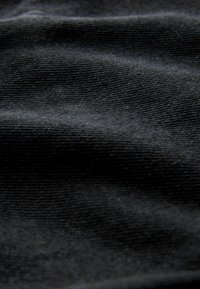 Tessuto nero con una consistenza liscia, che presenta trame fini e uniformi e una lucentezza sottile. Le pieghe creano ombre morbide sulla superficie.