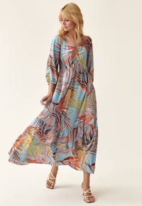 Blaues Maxikleid mit gestuftem Design, das farbenfrohe Palmenblattmuster in Rot, Gelb und Grün zeigt, mit Ballonärmel und gebundenem Ausschnitt.