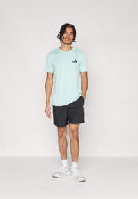 Lyseblå trenings T-skjorte med kort erm og svart logo, kombinert med svarte shorts. Antrekket har en avslappet passform og en jevn tekstur.