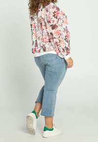 Chaqueta bomber floral en colores pastel con mangas abullonadas, combinada con unos vaqueros recortados azul claro y zapatillas blancas con detalles verdes.