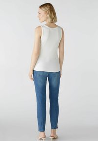 Weißes, geripptes Tanktop mit rundem Ausschnitt, kombiniert mit hellblauen, figurbetonten Jeans. Das Outfit hat eine glatte Textur und einen lässigen Stil.