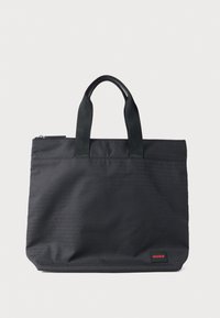 Čierna taška na rameno vyrobená z odolnej tkaniny s dvoma hornými rukoväťami. Má jemný reliéfny vzor loga a malú červenú značkovú etiketu.