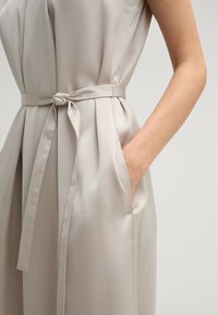 Lichtbeige satijnen jurk met een gestrikt zelfband, zijzakken en geplooide details. Glad textuur met een aansluitende bustier en een relaxte silhouet.