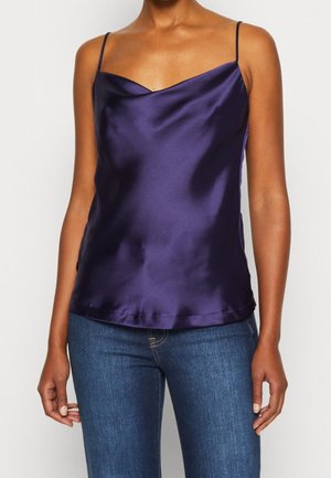 Camiseta de satén púrpura con escote drapeado y tirantes finos, combinada con jeans ajustados azules, textura suave, sin adornos.