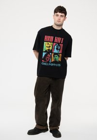 Black oversized t-shirt featuring colorful square graphic of band members with text "RED HOT CHILI PEPPERS," paired with brown wide-leg pants and black shoes.