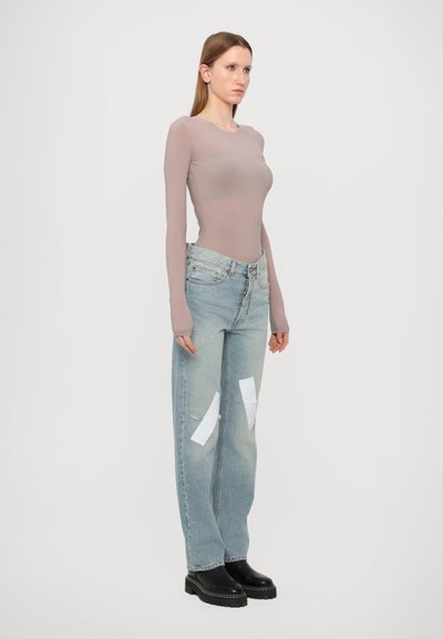 Langärmliges, eng anliegendes Oberteil in zartem Mauve mit gerippter Textur, kombiniert mit hoch taillierten, hellblauen Jeans mit weißen Flecken und einem entspannten Schnitt.
