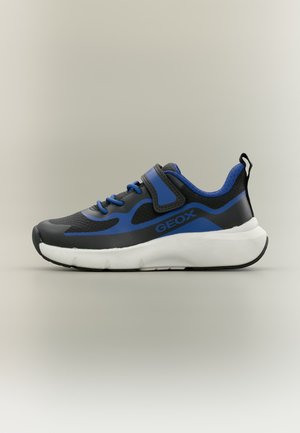 Baskets de sport noires et bleues avec semelle blanche, lacets bleus, sangle à scratch et languette à l’arrière du talon, vue de côté.