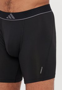 Calções atléticos pretos com uma cintura texturizada, apresentando um discreto logótipo "AEROREADY" em branco na perna e costuras planas para conforto.