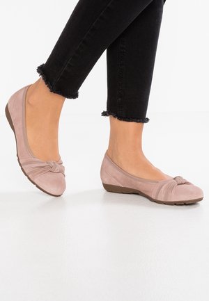 Lyserøde ruskindsballetsko med knude-detalje ved tæerne, blød rund form og en lav gummisål, kombineret med sorte jeans med frynset kant.