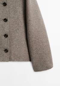 Cappotto grigio in lana con tessuto texturizzato, taglio dritto e bottoni neri sul davanti. La manica è leggermente affusolata.
