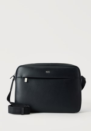 Sac messager en cuir noir texturé avec une bandoulière réglable et un petit logo BOSS argenté sur la fermeture éclair de la poche avant.