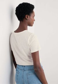 T-shirt a maniche corte di colore crema con una consistenza morbida, abbinato a jeans in denim azzurro a vita alta e con tasche posteriori visibili.