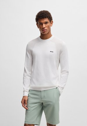 White knit sweater with round neckline, textured ribbed shoulders, and small black "BOSS" logo on the chest, paired with light green shorts.