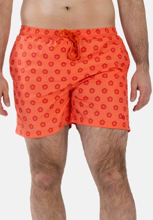 Mann trägt orangefarbene Badeshorts mit roten Blumenmustern und gebundener Kordel, von der Taille bis zur Mitte des Oberschenkels vor weißem Hintergrund gezeigt.