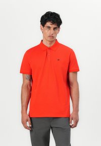 Rød polo-shirt lavet af glat stof, med en to-knaps placket, korte ærmer og et lille logo på venstre bryst.