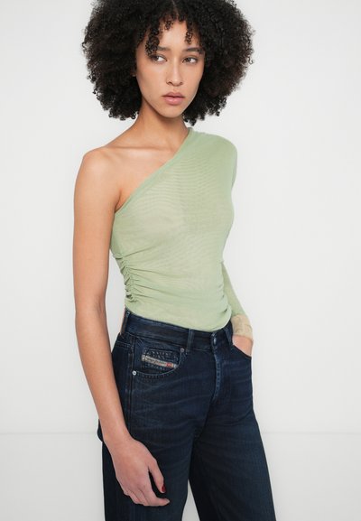 Haut vert clair à une épaule avec des détails froncés, associé à un jean denim bleu foncé avec une poche à rabat et un tissu texturé.