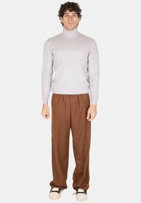 Maglione a collo alto grigio chiaro, pantaloni marroni con pieghe, sneaker bianche e nere. Tessuto morbido, vestibilità rilassata, design minimal.