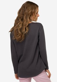 Camisa de manga larga gris oscuro con un corte relajado, dobladillo redondeado y textura suave, combinada con pantalones rosa claro.