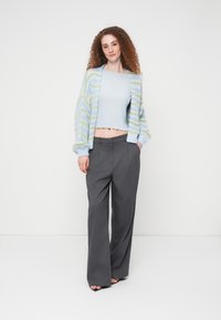 Πλεκτή ζακέτα σε παστέλ μπλε και πράσινες ρίγες, συνδυασμένη με ένα ανοιχτό μπλε ριμπ κορσέ και ψηλόμεσα γκρι παντελόνια με φαρδιά μπατζάκια.