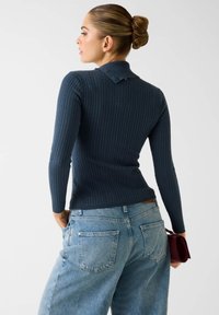Granatowy prążkowany top z długim rękawem i kołnierzykiem, w połączeniu z jasnoniebieskimi, wysokim stanem dżinsami. Dodatkiem jest mała bordowa kopertówka.