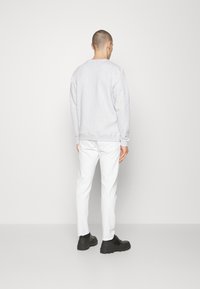 Szara bluza z długimi rękawami i ściągaczami, w zestawie z białymi spodniami i czarnymi butami. Prosty wzór, bez widocznych wzorów ani logo.