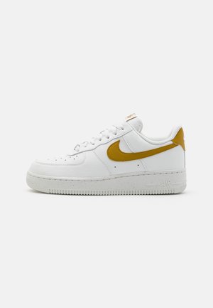 Nike Air Force 1 sneakers in white leather with a yellow Swoosh, textured upper, round toe, white rubber sole, and perforated detailing.