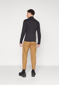 Black ribbed long-sleeve top with a collar, paired with tan tapered pants. The outfit includes black footwear and subtle branding on the pants.