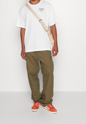 Camiseta de algodón blanca con diseño gráfico, pantalones cargo verde olivo con bolsillos y zapatillas naranjas con rayas blancas.