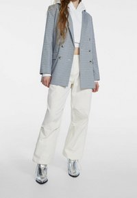 Szary żakiet w kratę typu double-breasted, biały krótkie bluza z kapturem pod spodem, białe szerokie spodnie oraz srebrne botki za kostkę z ostrym noskiem.