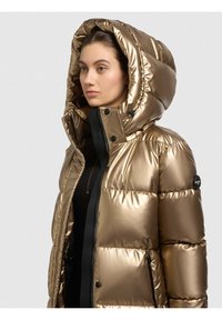 Metallic-goldfarbene Steppjacke mit großer Kapuze, Reißverschluss und schwarzen Akzenten. Horizontal gesteppte Optik und Seitentaschen. Glatte Textur.