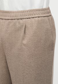 Pantalon beige texturé avec taille élastique et poches latérales, porté avec un haut blanc rentré.