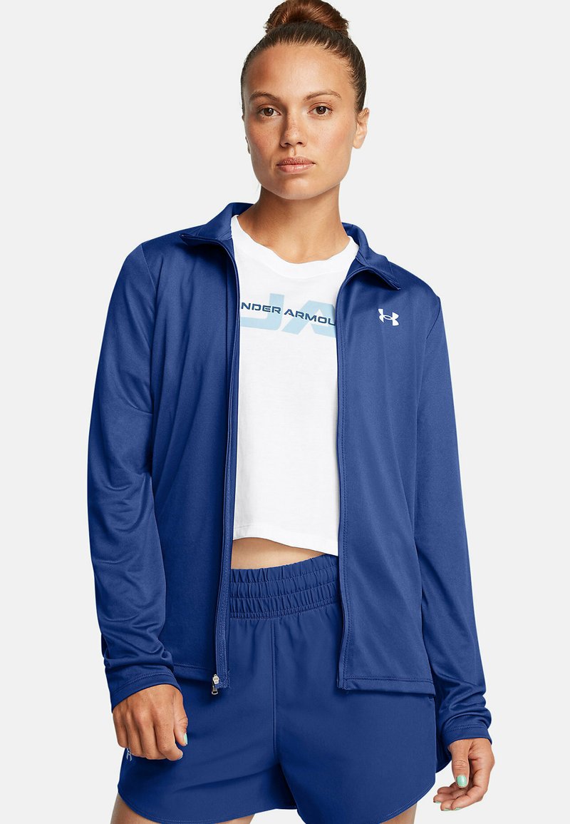 Navy krāsas sporta zip jakas, izgatavotas no viegla, gluda auduma, kombinētas ar īsu balto kreklu un atbilstošām šortiem, ar elastīgu jostu.