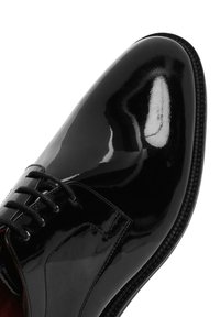 Glanzende zwarte leren nette schoen met gesloten vetering en afgeronde neus, met gedetailleerde stiksels en gepolijste oppervlakreflectie.