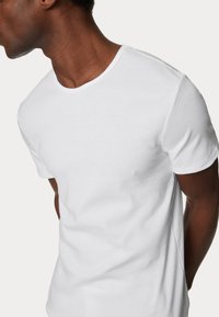 Camiseta de algodón blanca con mangas cortas, un cuello redondo y una textura suave. Diseño simple sin logotipos ni patrones visibles.