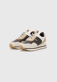 Sneaker beige e marroni con una parte superiore in mesh testurizzato, dettagli in suede e particolari bianchi. Presentano una suola spessa e rigata con un accento dorato.