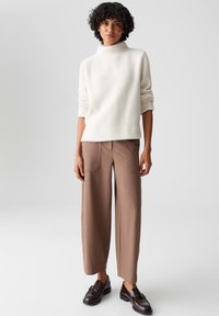 Maglione cremoso e strutturato con collo alto, abbinato a pantaloni larghi marroni con tasche posteriori. Il modello indossa scarpe scure.