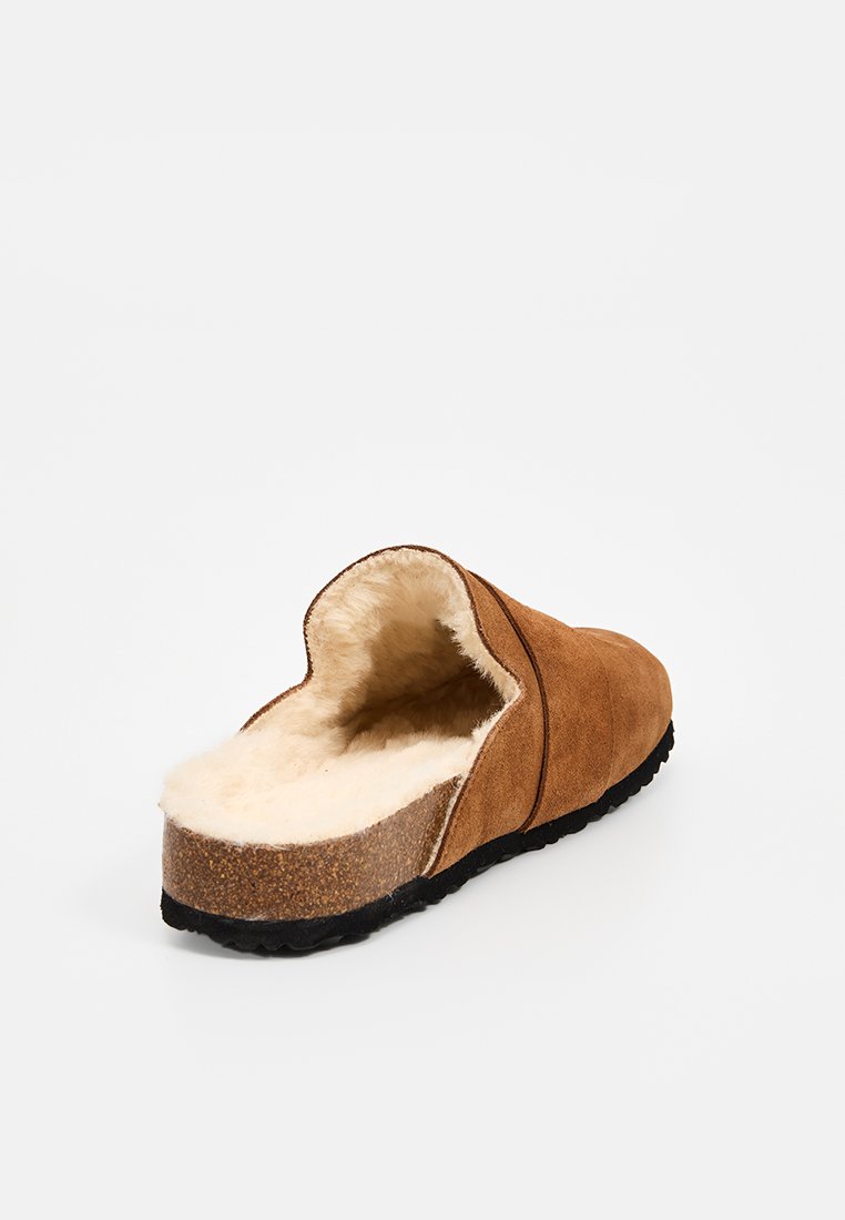 Bruine suede slof met voering van schapenvacht, open achterkant ontwerp en een gestructureerde rubberen zool. Laag profiel, ronde vorm voor comfort.