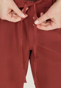 Bordeauxfärgade joggers med elastisk midja och dragsko. Tyget är slätt med en lätt lyster och har två synliga sid sömmar.