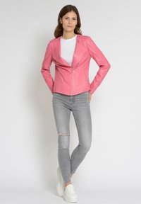 Lyserød faux læderjakke med notched krave, lynlås lukning og tætsiddende design. Sættes sammen med lysegrå jeans og hvide sneakers.