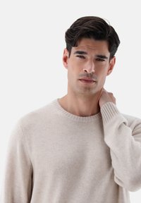 Maglione beige lavorato a maglia con collo a girocollo a coste e maniche lunghe, caratterizzato da una texture morbida e una silhouette aderente.