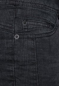 Jean en denim noir avec motif, doté d'une poche avant avec boutons en métal noir et détails de coutures contrastantes.