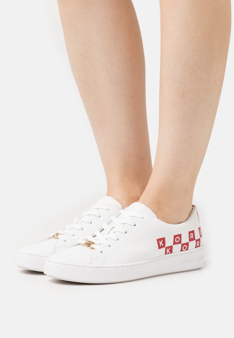 Baskets blanches en cuir avec inscription "KORS" rouge et accents à motifs damiers, dotées d'un laçage plat et de détails subtils en or.