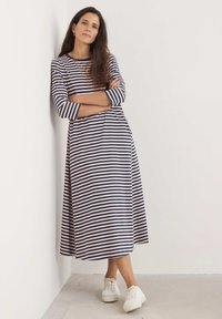 Pruhované dlouhé rukávy šaty v námořnické a krémové barvě, s volným střihem a délkou ke kolenům, spárované s bílými teniskami. Měkká bavlněná látka.