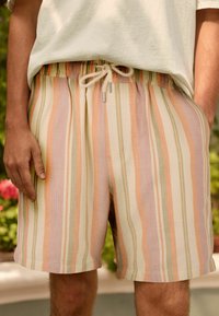 Pantalones cortos ligeros a rayas en colores pastel (durazno, verde, beige), con una cinturilla elástica con cordón y bolsillos laterales.