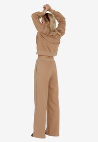 Brązowa, krótką bluza z długim rękawem w połączeniu z dopasowanymi, szerokimi spodniami dresowymi, oba wykonane z miękkiej tkaniny. Charakteryzuje się luźnym krojem oraz bocznymi kieszeniami.