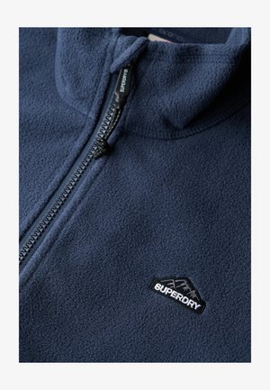 Marineblauwe fleece jas met een half-ritsontwerp, textuur oppervlak en een zwart geborduurd logo met bergdetail op de linkerkant van de borst.