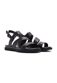 Black leather sandals feature multiple wide straps, an adjustable ankle buckle, and a flat rubber sole with slight tread for grip.