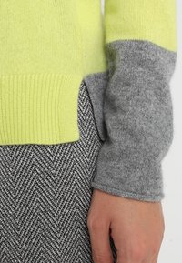 Tröja i ljusgul och grå material, med ribbat stickat mönster, som har en färgblockerad design och ett sidoklyvningsdetalj.